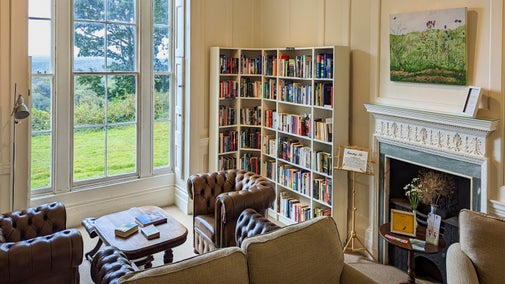 Internal view of the library at Leith Hill Place, with two leather sofas in the foreground, bookshelves at either side and a long window looking over the south terrace